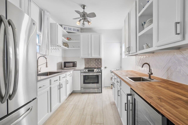 kitchen with appliances with stainless steel finishes, sink, white cabinets, butcher block countertops, and wine cooler