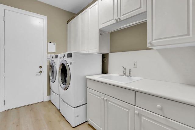 clothes washing area with washing machine and clothes dryer, light hardwood / wood-style flooring, cabinets, and sink