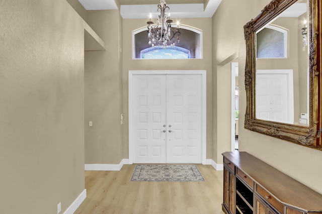 foyer entrance with an inviting chandelier, a towering ceiling, and light hardwood / wood-style flooring