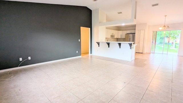 unfurnished living room featuring a notable chandelier, high vaulted ceiling, and light tile patterned flooring