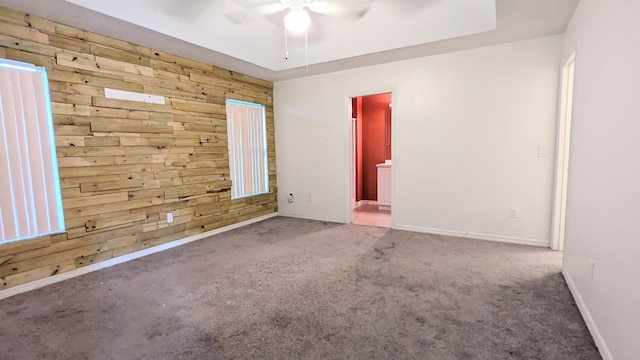 spare room featuring carpet, wooden walls, and ceiling fan