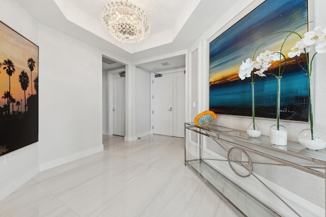 corridor featuring a tray ceiling and a chandelier