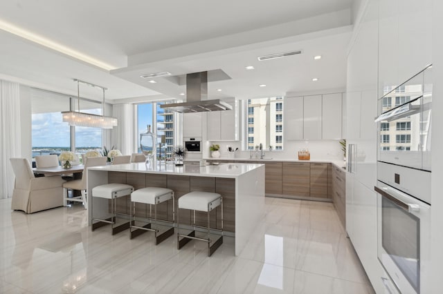 kitchen featuring white cabinets, sink, island range hood, a large island, and decorative light fixtures