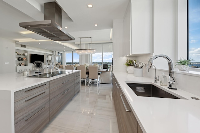 kitchen with wall chimney exhaust hood, pendant lighting, black electric cooktop, sink, and white cabinets