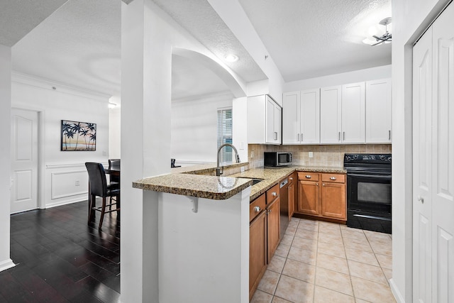 kitchen with light stone counters, stainless steel appliances, white cabinets, kitchen peninsula, and a textured ceiling