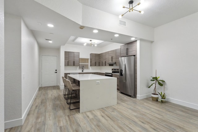 kitchen featuring a kitchen island, a textured ceiling, stainless steel appliances, light wood-type flooring, and a kitchen bar