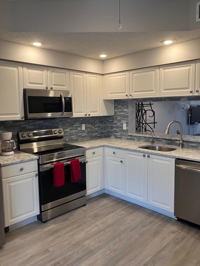 kitchen featuring sink, light hardwood / wood-style flooring, a textured ceiling, appliances with stainless steel finishes, and white cabinetry