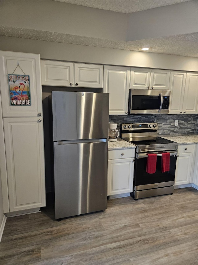 kitchen featuring backsplash, white cabinets, light wood-type flooring, and appliances with stainless steel finishes