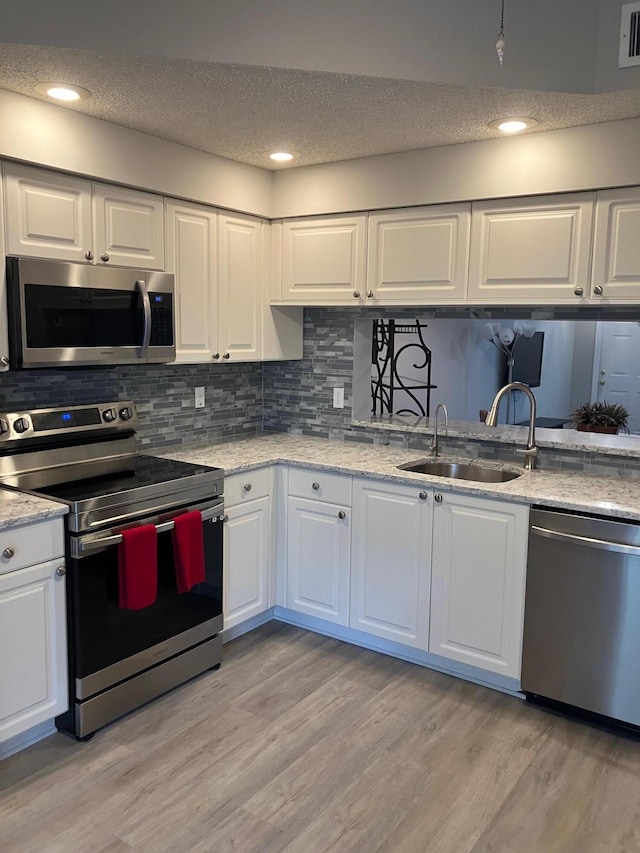 kitchen with appliances with stainless steel finishes, tasteful backsplash, sink, white cabinets, and light hardwood / wood-style floors