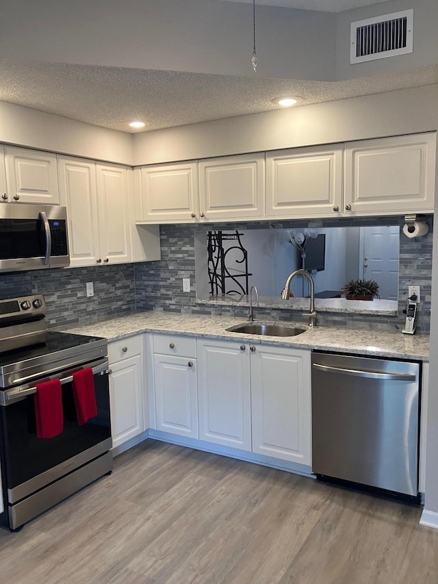 kitchen with white cabinets, sink, decorative backsplash, light wood-type flooring, and appliances with stainless steel finishes