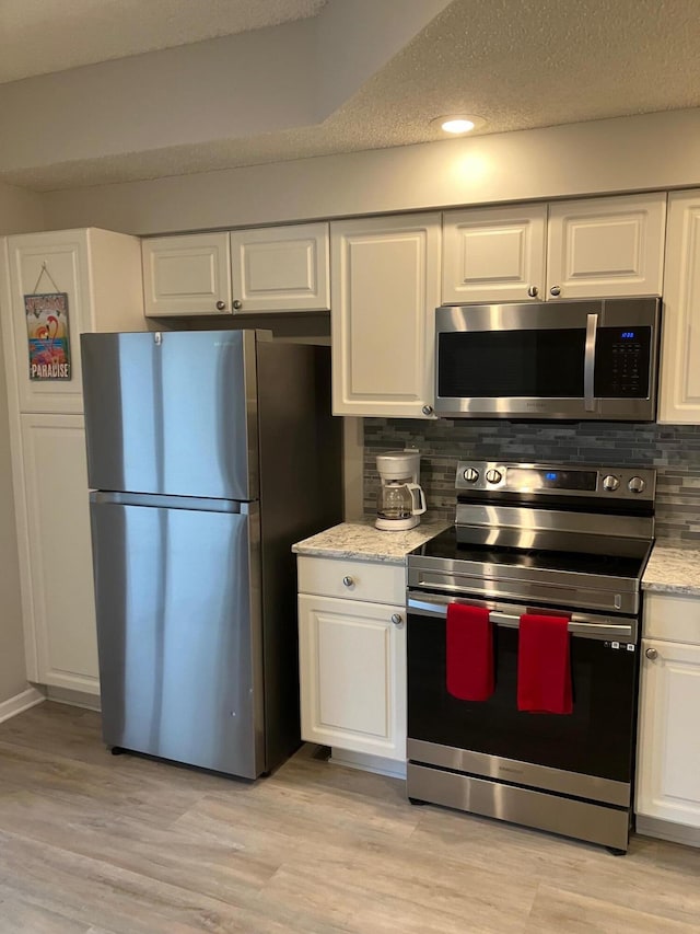 kitchen with backsplash, light stone counters, stainless steel appliances, light hardwood / wood-style flooring, and white cabinetry