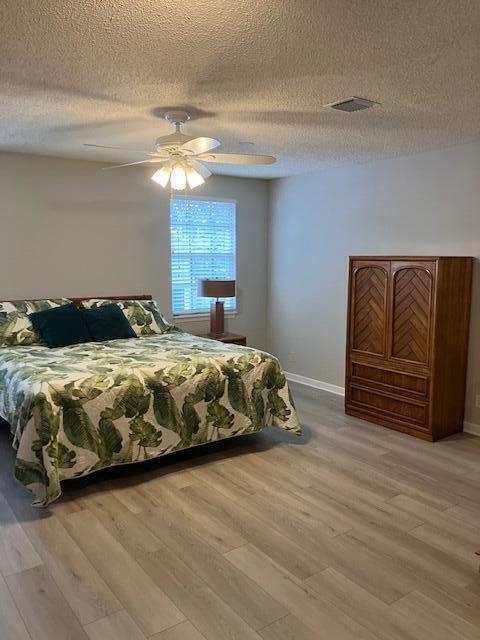 bedroom with ceiling fan, light hardwood / wood-style floors, and a textured ceiling