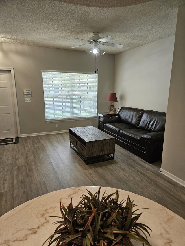 living room featuring ceiling fan, dark wood-type flooring, and a textured ceiling