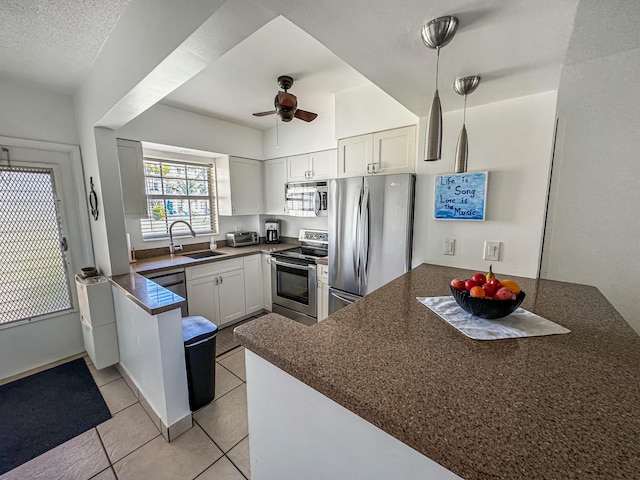 kitchen featuring dark countertops, appliances with stainless steel finishes, light tile patterned flooring, a sink, and a peninsula