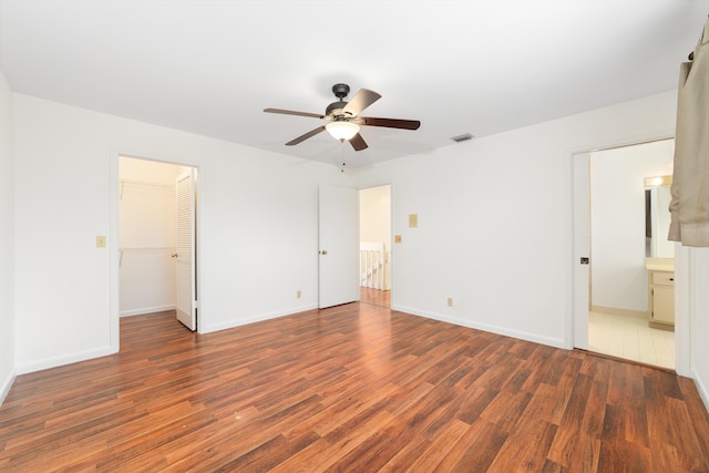 unfurnished bedroom featuring dark hardwood / wood-style flooring, a spacious closet, ceiling fan, ensuite bath, and a closet