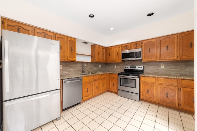 kitchen featuring sink, light tile patterned floors, appliances with stainless steel finishes, backsplash, and light stone countertops