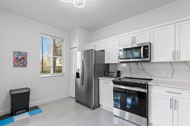 kitchen featuring tasteful backsplash, light stone counters, white cabinetry, a textured ceiling, and stainless steel appliances