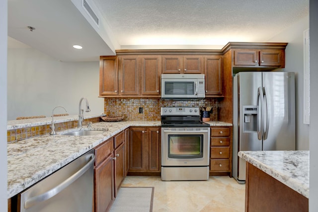 kitchen featuring light stone counters, a textured ceiling, tasteful backsplash, sink, and appliances with stainless steel finishes