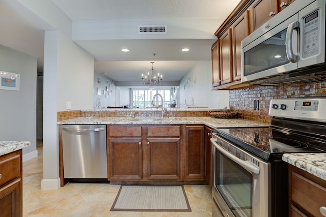 kitchen with appliances with stainless steel finishes, light stone counters, tasteful backsplash, sink, and a notable chandelier