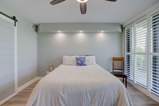 bedroom with a barn door, hardwood / wood-style floors, and ceiling fan