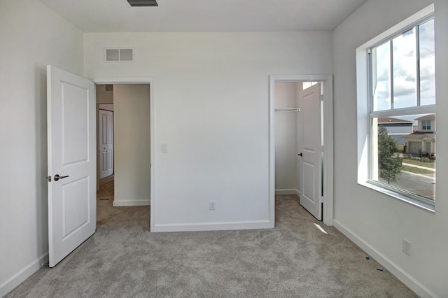 unfurnished bedroom with a spacious closet, multiple windows, and light carpet