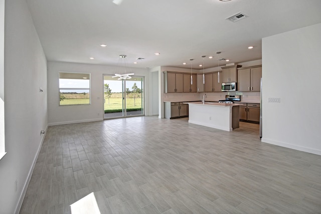 kitchen featuring a kitchen island with sink, stainless steel appliances, sink, hanging light fixtures, and light hardwood / wood-style flooring