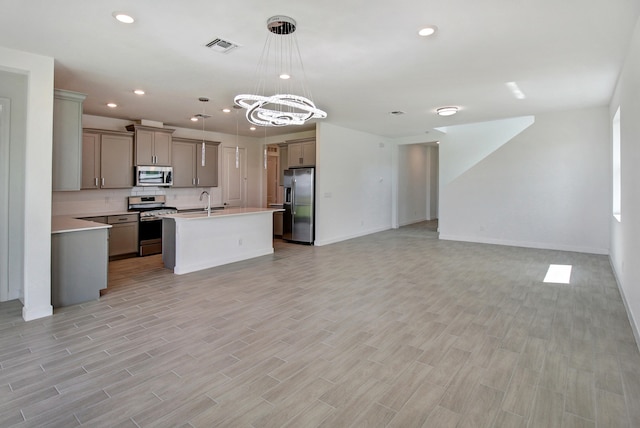 kitchen with a center island with sink, decorative light fixtures, appliances with stainless steel finishes, and light hardwood / wood-style flooring