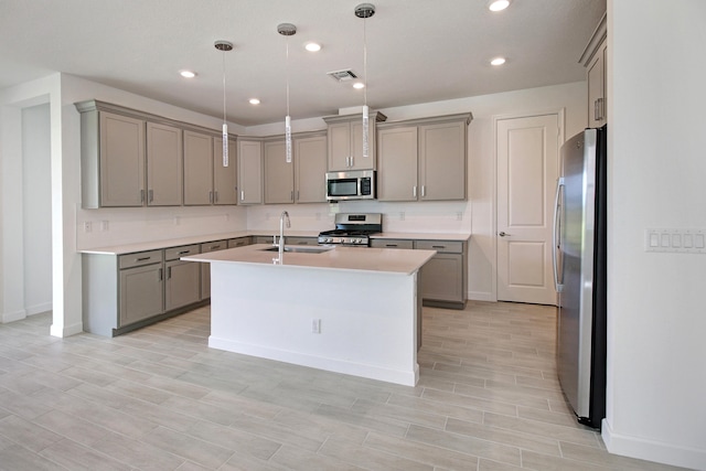 kitchen featuring an island with sink, stainless steel appliances, sink, hanging light fixtures, and light hardwood / wood-style flooring