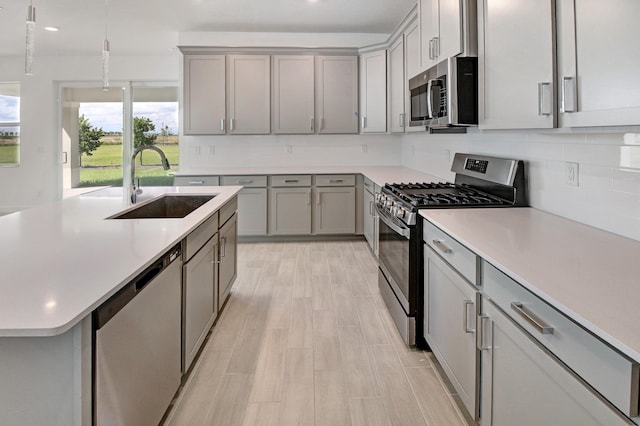 kitchen with sink, pendant lighting, light hardwood / wood-style flooring, appliances with stainless steel finishes, and backsplash