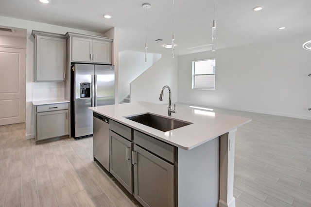 kitchen with gray cabinetry, sink, light hardwood / wood-style floors, appliances with stainless steel finishes, and a center island with sink