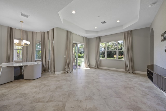 spare room with a textured ceiling, a raised ceiling, and a notable chandelier