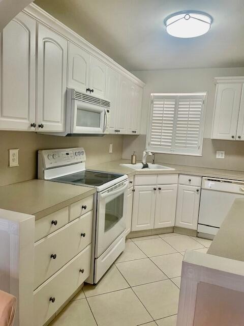 kitchen featuring light tile patterned floors, white cabinets, sink, and white appliances