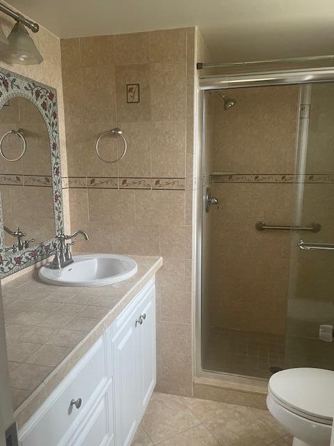 bathroom with tile patterned floors, a shower with shower door, tile walls, and vanity