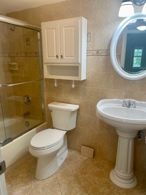 bathroom with tile walls, bath / shower combo with glass door, tile patterned floors, and toilet