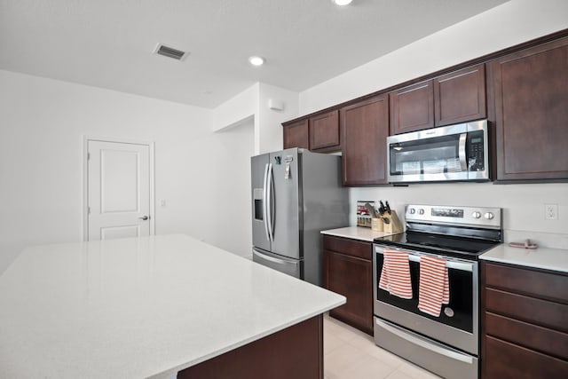 kitchen with dark brown cabinetry, appliances with stainless steel finishes, a kitchen island, and light tile patterned flooring