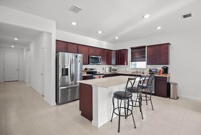 kitchen with appliances with stainless steel finishes, a kitchen island, a breakfast bar area, and light tile patterned floors