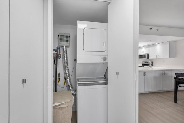 laundry area with light hardwood / wood-style flooring and stacked washer and clothes dryer