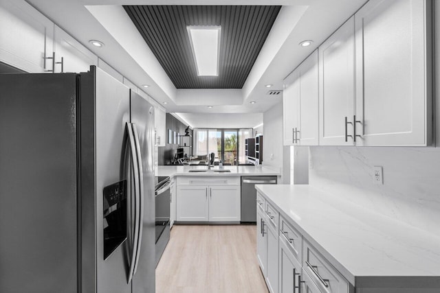 kitchen featuring white cabinets, a raised ceiling, stainless steel appliances, light wood-type flooring, and sink