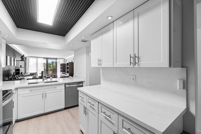 kitchen featuring light hardwood / wood-style floors, white cabinetry, backsplash, stainless steel appliances, and a tray ceiling