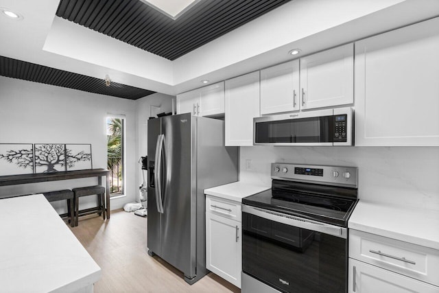 kitchen with appliances with stainless steel finishes, decorative backsplash, white cabinetry, a tray ceiling, and light hardwood / wood-style flooring