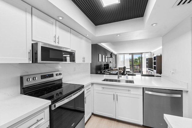 kitchen featuring light hardwood / wood-style floors, sink, white cabinets, backsplash, and appliances with stainless steel finishes