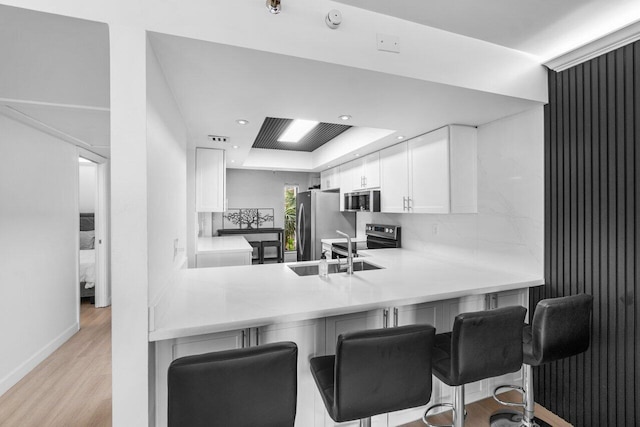 kitchen with appliances with stainless steel finishes, a kitchen bar, white cabinets, and kitchen peninsula