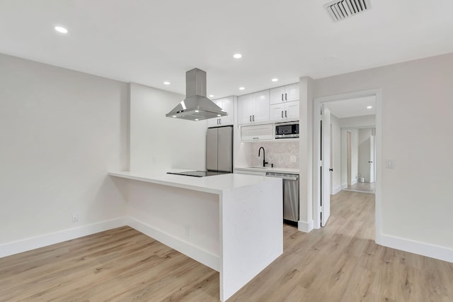 kitchen featuring light wood-type flooring, tasteful backsplash, white cabinetry, island exhaust hood, and stainless steel appliances