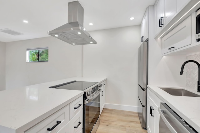 kitchen with appliances with stainless steel finishes, white cabinets, light stone countertops, island exhaust hood, and light hardwood / wood-style flooring