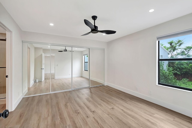 unfurnished bedroom featuring multiple windows, light wood-type flooring, ceiling fan, and a closet