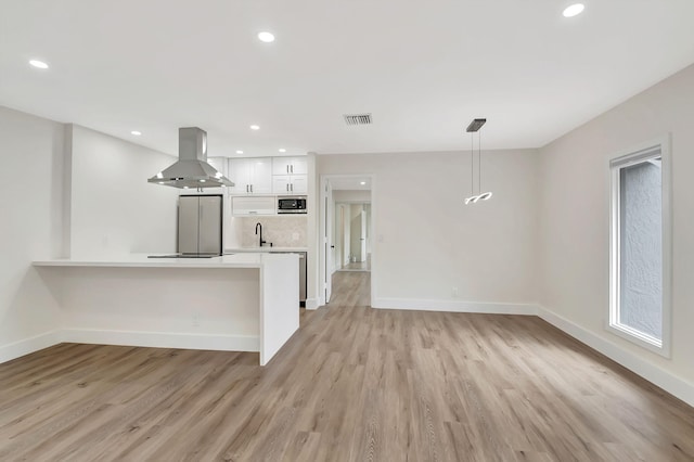 kitchen featuring white cabinets, kitchen peninsula, light wood-type flooring, decorative light fixtures, and extractor fan