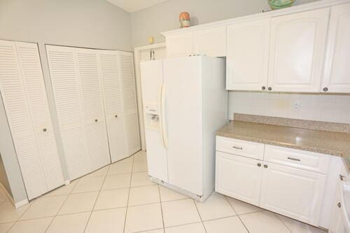 kitchen with white cabinetry, white fridge with ice dispenser, and light tile patterned floors