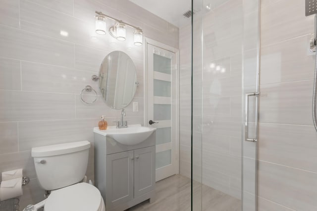 bathroom featuring walk in shower, tile walls, vanity, and toilet