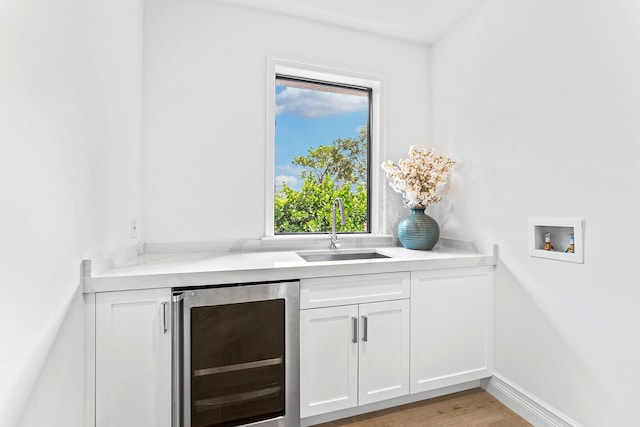 bar featuring wine cooler, light hardwood / wood-style floors, sink, and white cabinets