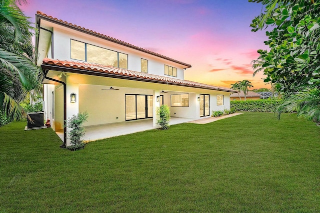 back house at dusk with a patio, central AC, and a lawn